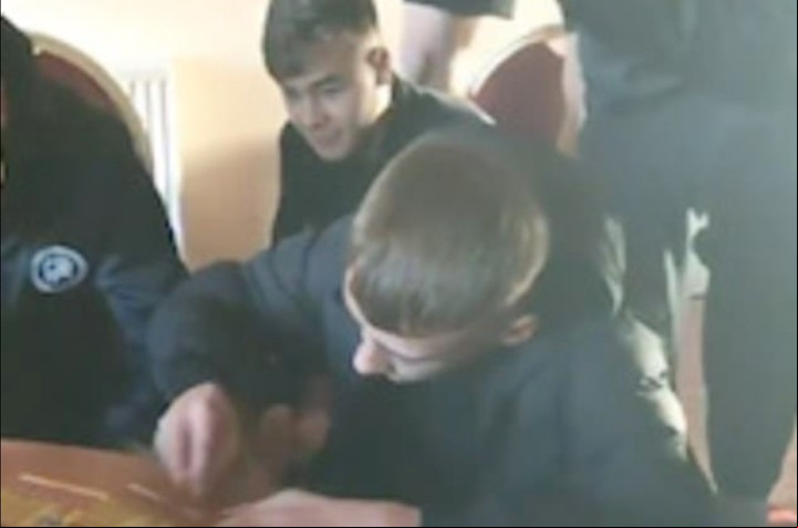 Reece que raspa la tarjeta en una mesa sin saber que sus compañeros estaban complotados en la broma (Captura de video).