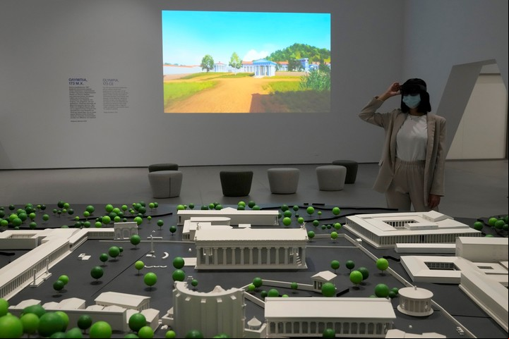 La supervisora del museo Xenia Vlahou usa auriculares HoloLens de realidad mixta mientras se para frente a un modelo a escala de la antigua Olimpia en el Museo Olímpico de Atenas. (AP Photo/Thanassis Stavrakis)