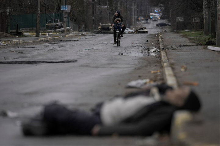 Un hombre lleva en bicicleta a su hijo aproximándose a un cadáver en una calle de Bucha, en las afueras de Kiev. Tras el repliegue ruso, apareció el horror. Foto: AP