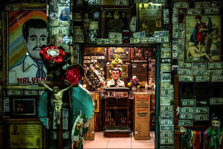 Ofrendas de flores, velas, fotos y billetes de dólar en un altar a Jesús Malverde, un "narco-santo", en Culiacán. Foto de Meridith Kohut para The New York Times.